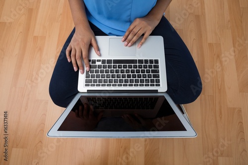 Female executive using laptop while sitting on wooden floor