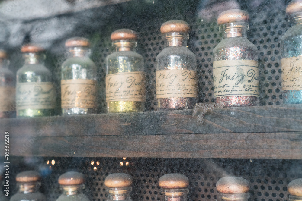 Closeup set of colorful fairy dust glitters in bottles isolated on dusty vintage display Closeup set of colorful fairy dust glitters in bottles isolated on dusty vintage display