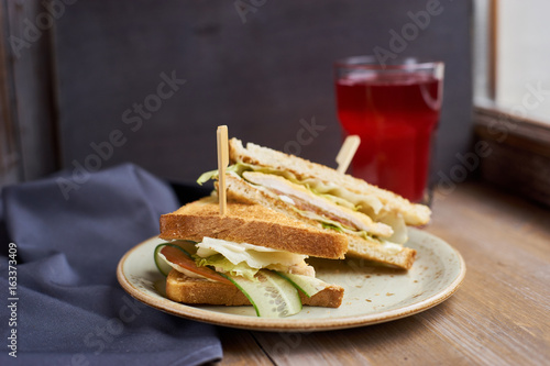 Two Club sandwich with cheese, ham, lettuce and cucumber on plate and glass of cranberry juice on wooden table