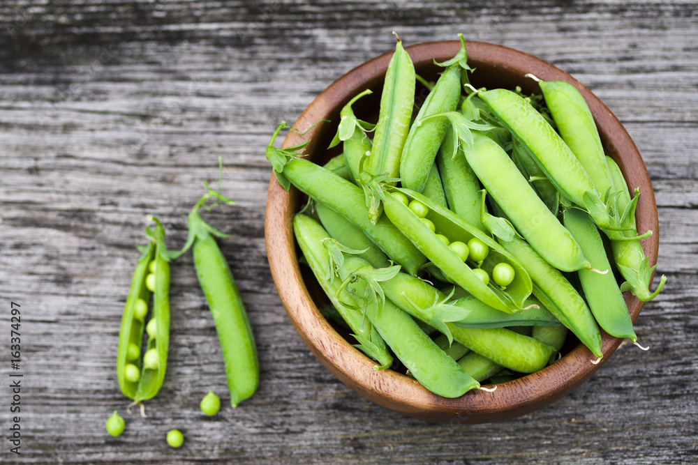 Pods of green peas in a round plate on an old wooden surface, top view Pods of green peas in a round plate on an old wooden surface, top view