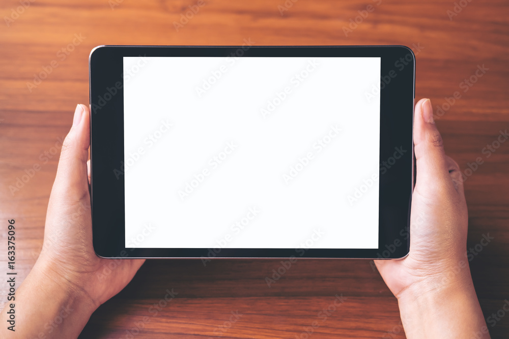 Mockup image of hands holding black tablet pc with blank white screen on vintage wooden table background
