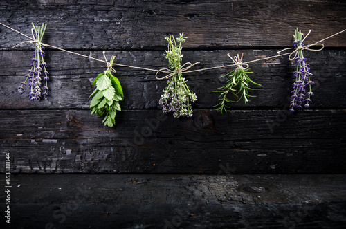 Lavender flowers, rosemary, mint, thyme, melissa with old scissors on a black wooden table. Burnt wood. Spa and cosmetic or cooking background.