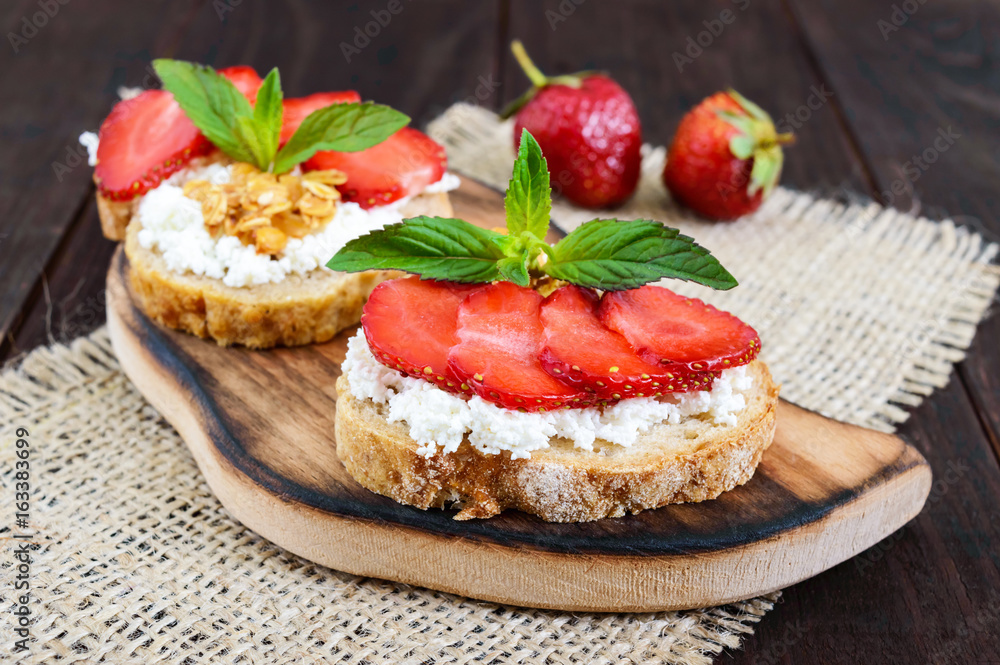 A small bruschetta with curd and fresh strawberries on a dark wooden background. Proper nutrition. A small bruschetta with curd and fresh strawberries on a dark wooden background. Proper nutrition.