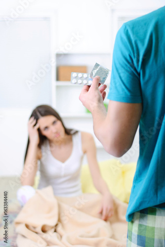 Young man showing a woman a condom and pills for headaches while she abide head