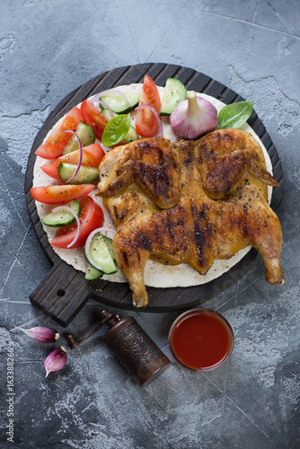 Top view of roasted chicken tapaka served with fresh vegetables, vertical shot over grey stone background photo