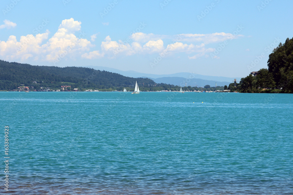 a large lake with turquoise water and a yacht with a white sail