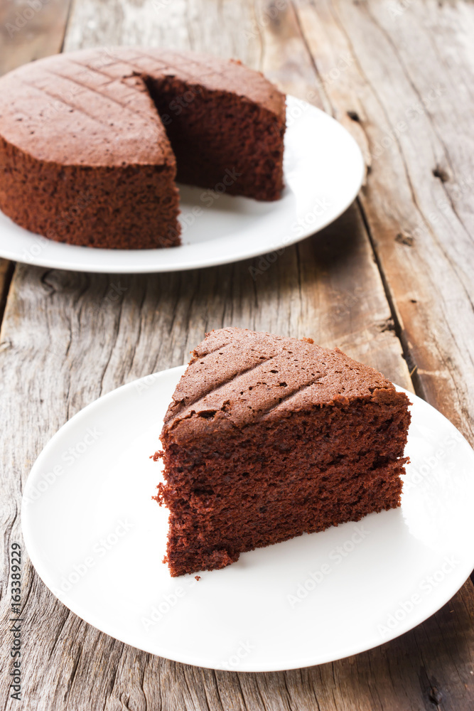 Sliced homemade chocolate cake on white plate over wooden table. Sliced homemade chocolate cake on white plate over wooden table.
