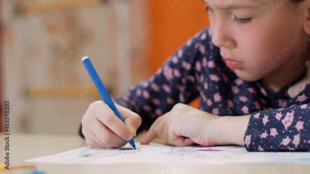 A little girl at the desk draws a blue felt-tip pen. close-up A little girl at the desk draws a blue felt-tip pen. close-up
