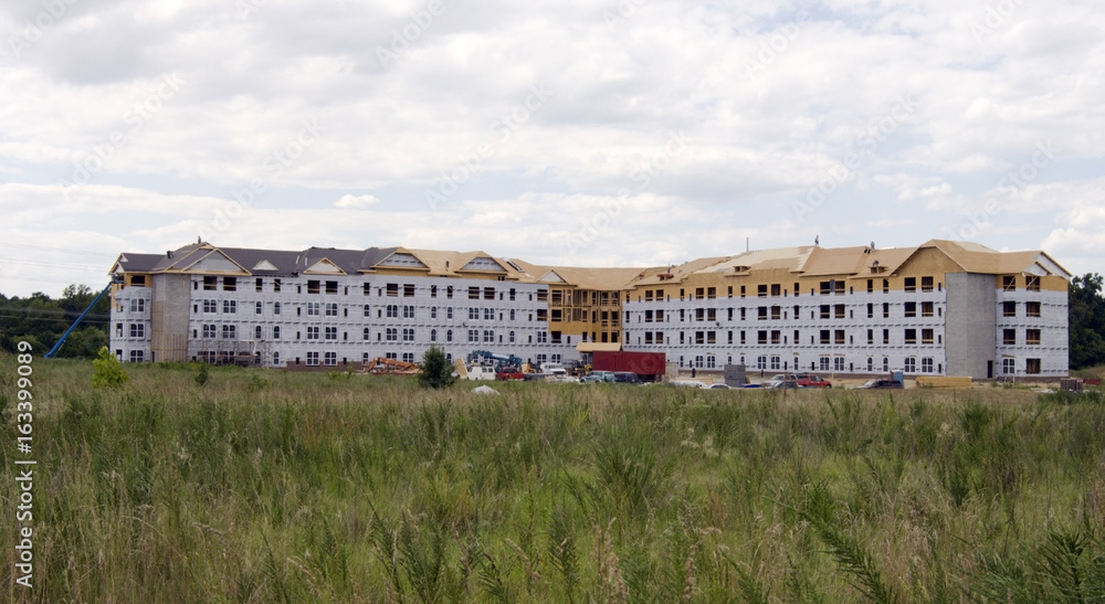 Housing construction with foreground field and clouds sky.