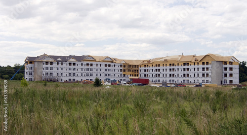 Housing construction with foreground field and clouds sky.