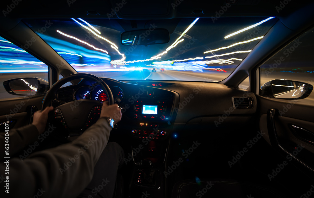 Hands on the wheel the car moves with fast speed on the highway at night. Blurred road with lights with a car at high speed.