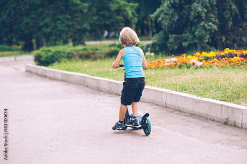 Fototapeta Naklejka Na Ścianę i Meble -  A little boy is riding a scooter in the park