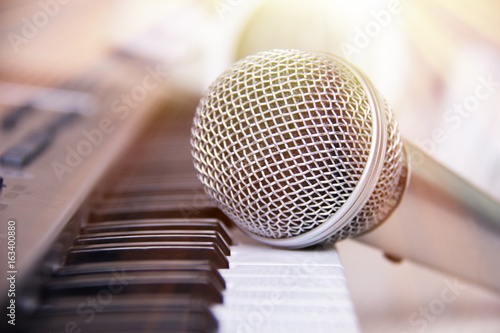 Close up on a microphone during recording session with a singer, piano in the background, music studio, light leak style.