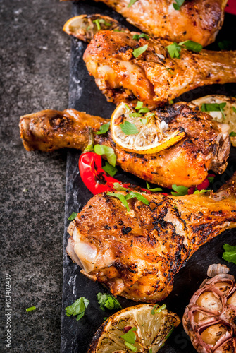Summer food. Ideas for barbecue, grill party. Chicken legs, wings grilled, fried on fire. With hot chili pepper, lemon and bbq sauce. Dark stone table, Copy space