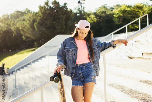 Fotografie Young girl with longboard in the park at sunrise or sunset