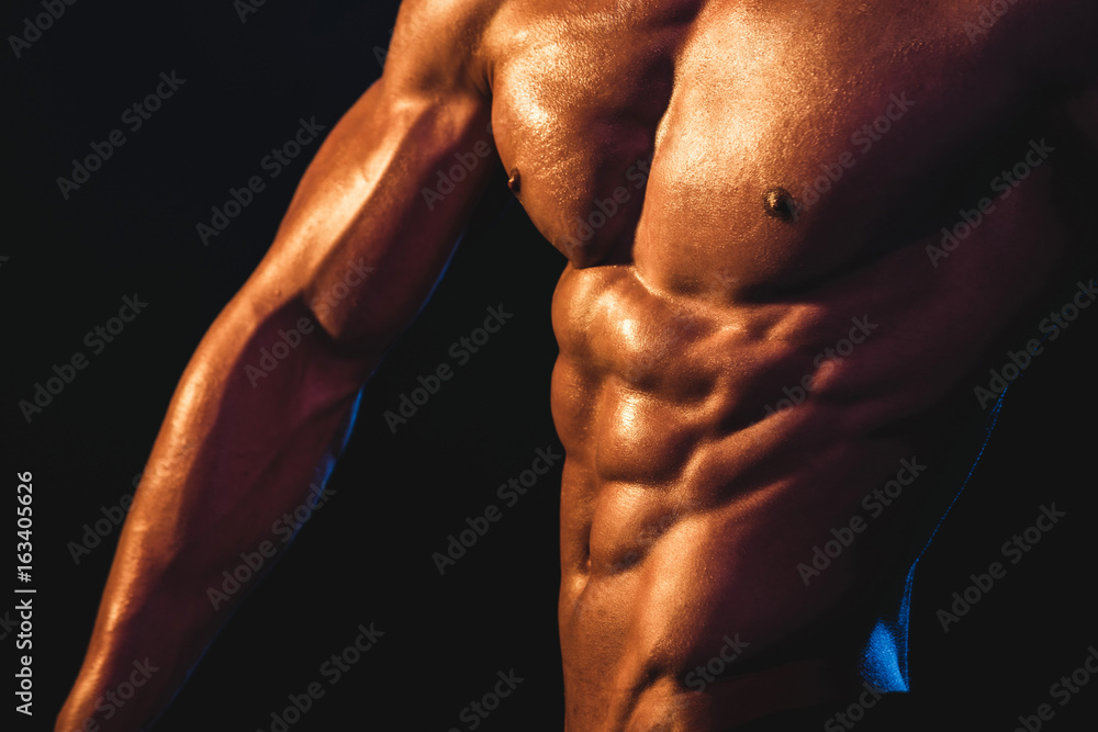Chest, arm and abs of young athlete close up. Strong bodybuilder shows his body. Unrecognizable Strong bald bodybuilder with six pack. Bodybuilder man with perfect abs flexing his muscles 