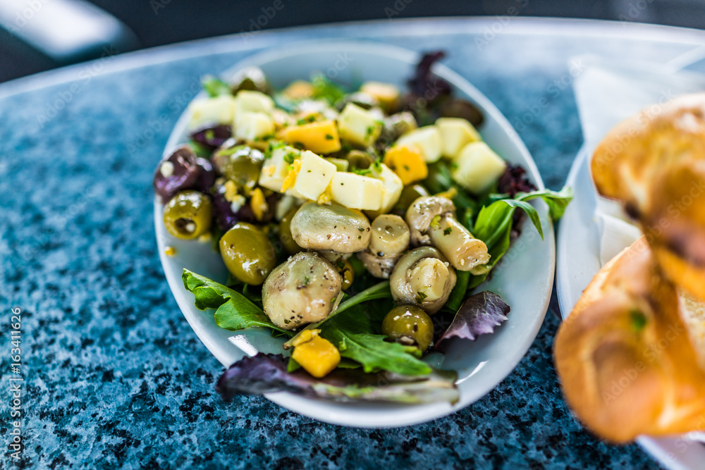 Macro closeup of salad on plate in restaurant with mushrooms, cheese squares, olives and greens