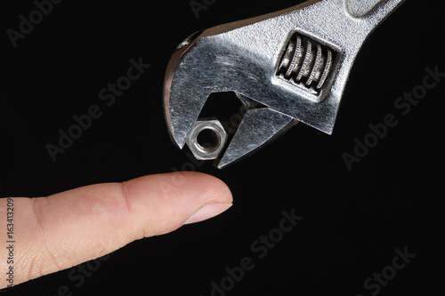 Obraz na płótnie Wrench puts the nut on finger on black background