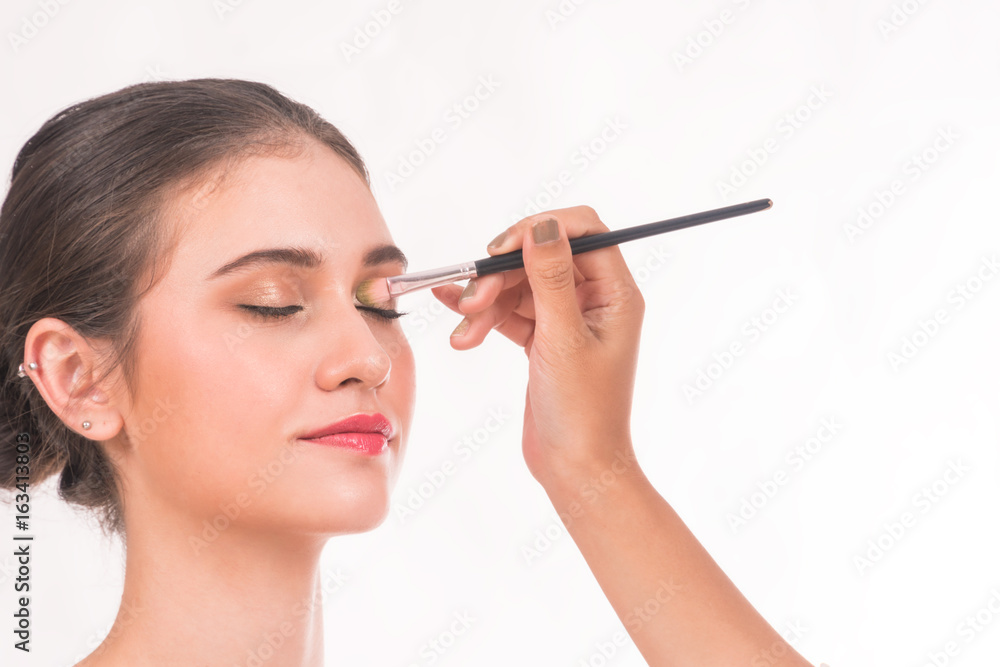 Makeup artist applying eyeshadow for beautiful young woman on white background. Makeup artist applying eyeshadow for beautiful young woman on white background.