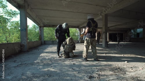 Two men in uniform attacking terrorists and freeing hostage inside of ruined building.