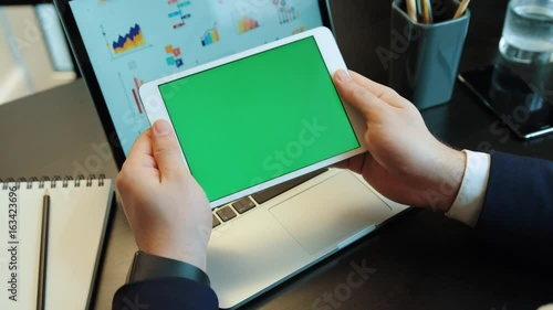 Young man hands using tablet with green screan on the laptop backgroud with diagrams. Chroma key. Horizontal positiion. photo