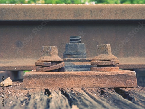 Detail of rusty screws and nut on old railroad track. Rooten wooden tie with rusty nuts and bolts. photo