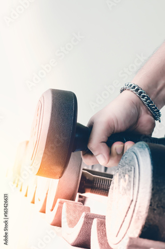 strong man's hand takes a heavy dumbbell in gym