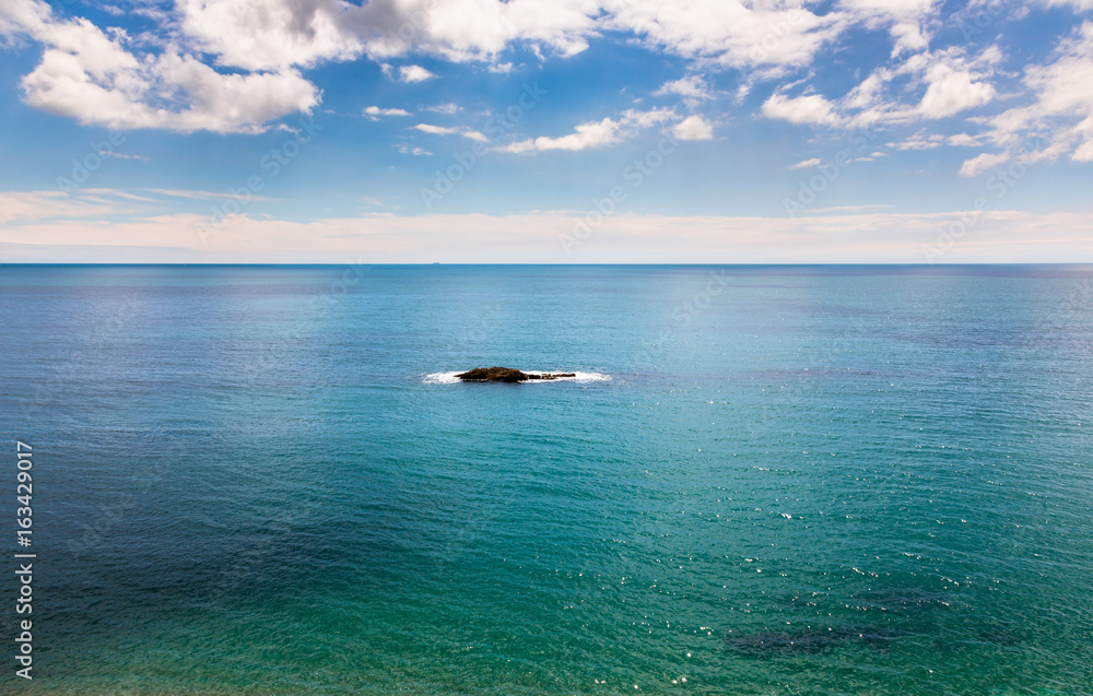 Single rocky island on calm azure blue sea.