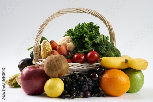 Close-up composition with vegetables and fruit in wicker basket isolated on white background with copy space. Healthy eating and detox concept. Vegetarian food.