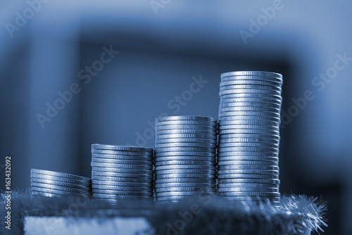 Stack of gold coin on artificial grass in pot, on wooden table.