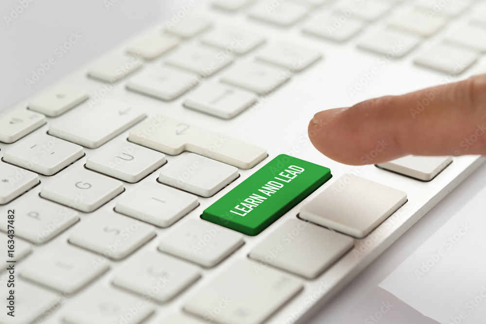 Computer Keyboard Concept: Hand pushing green LEARN AND LEAD keyboard button Computer Keyboard Concept: Hand pushing green LEARN AND LEAD keyboard button
