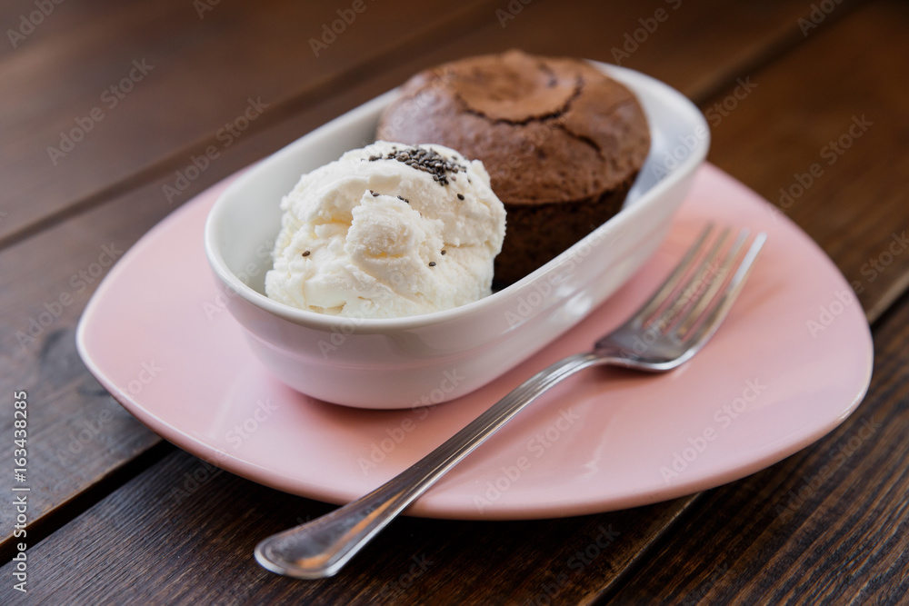 Chocolate lava cake with ice cream covered with poppy seeds, in a white bowl, on a pink plate, fork near by. Wooden table. Selective focus, small depth of field. Chocolate lava cake with ice cream covered with poppy seeds, in a white bowl, on a pink plate, fork near by. Wooden table. Selective focus, small depth of field.