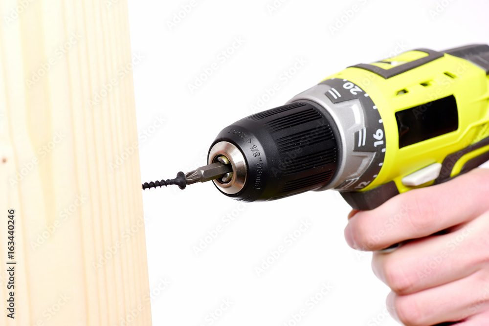 Screwdriver in yellow color in mans hand near wooden board