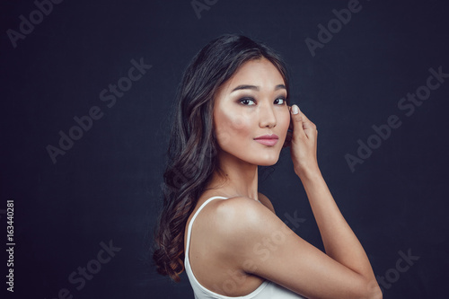 Portrait of a beautiful asian woman with makeup and light curls on black background.