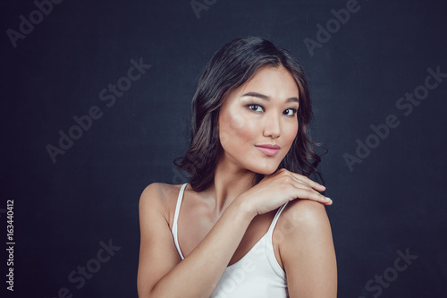 Portrait of a beautiful asian woman with makeup and light curls on black background.