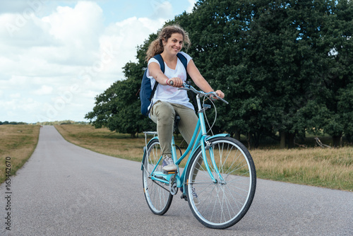 Smiling pretty young woman riding bike in a country road in the park