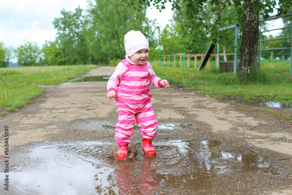 Happy smiling little 1 years baby girl in wellingtons walking after rain Happy smiling little 1 years baby girl in wellingtons walking after rain
