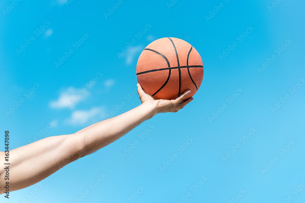 cropped shot of hand holding basketball ball against clear blue sky