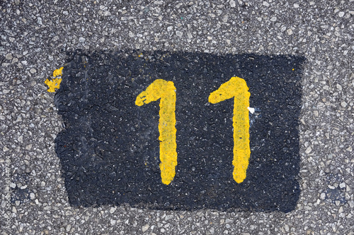 Yellow imprint of the number eleven on an asphalt pavement. photo