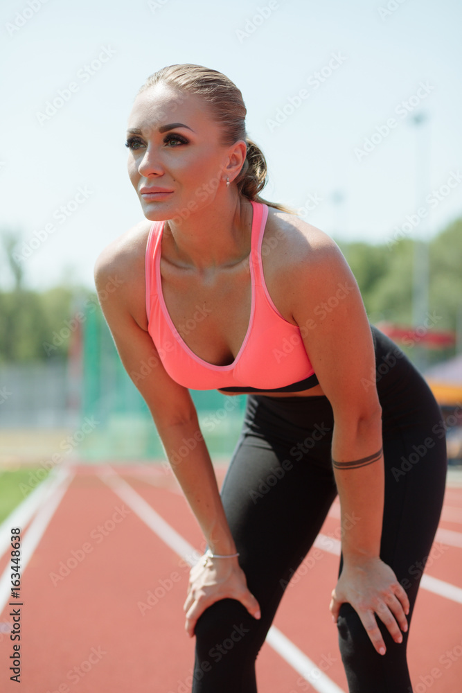 Young sporty woman sprinter athlete in sportswear resting after run on stadium track Young sporty woman sprinter athlete in sportswear resting after run on stadium track