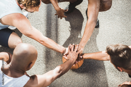 overhead view of basketball team holding hands on basketball ball on court photo