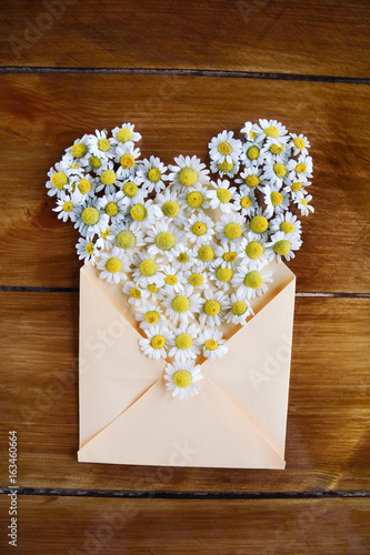 Heart made of chamomile flowers on a wooden background
