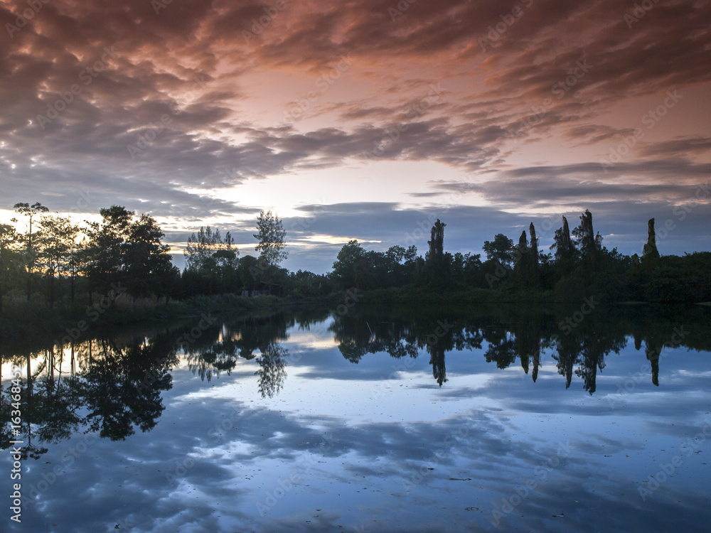 Fototapeta premium The setting sun and clouds reflect in a lake in east Thailand (filtered).