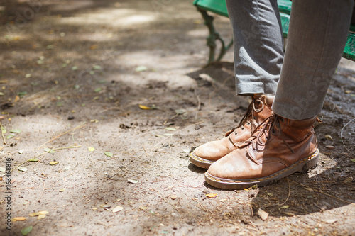 Young fashion hipster man's legs in brown leather boots and wearing gray jeans with both feet stepped on the floor ground, concept of fashion and vintage lifestyle.