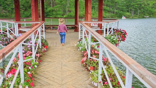 Little Girl Walks Barefoot on Bridge to Lake Pavilion in Park photo