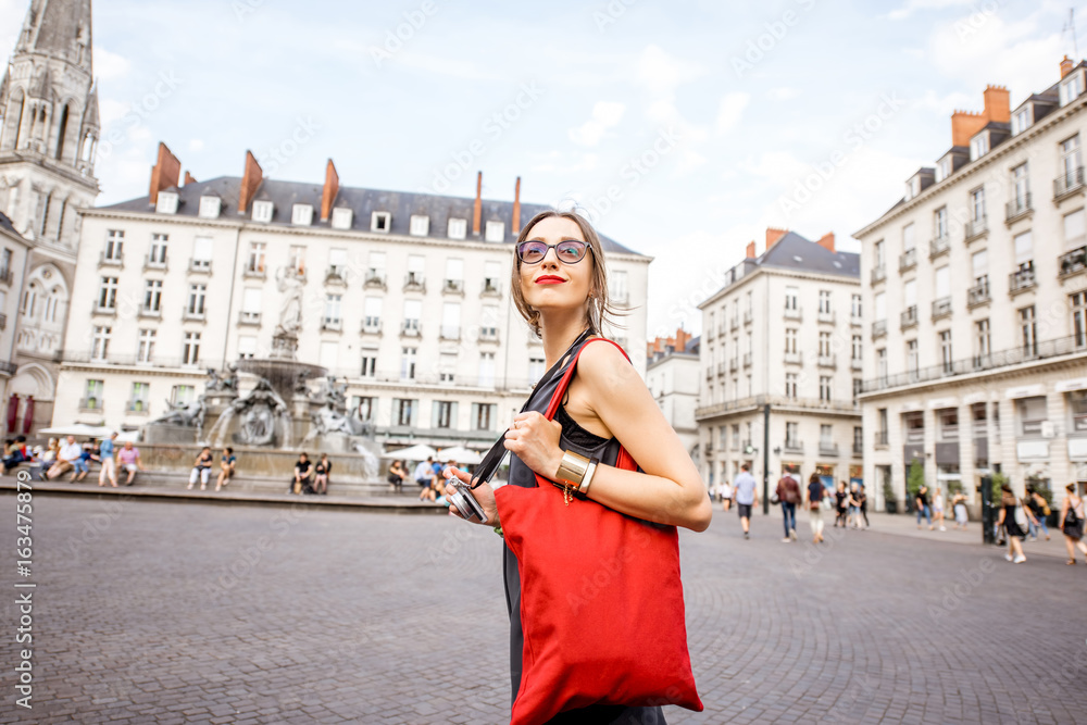 Young woman tourist with photo camera and red bag walking on the Royal main square in Nantes city, France