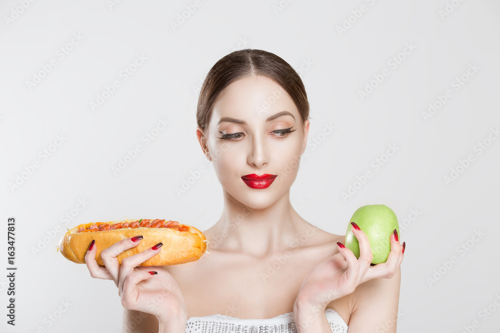 Woman compare tasty unhealthy burger sandwich hotdog in hand and green apple getting ready to eat healthy food isolated on a white background, healthy eating concept Woman compare tasty unhealthy burger sandwich hotdog in hand and green apple getting ready to eat healthy food isolated on a white background, healthy eating concept