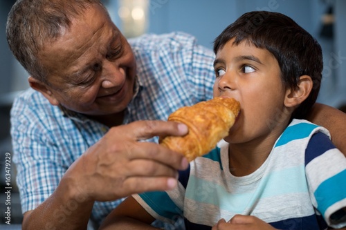 Grandfather feeding croissant to grandson