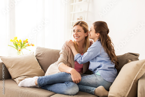 happy girl whispering secret to her mother at home