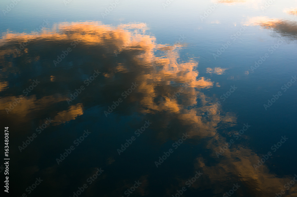 Reflection on the surface of calm water - orange clouds and blue sky during sunset